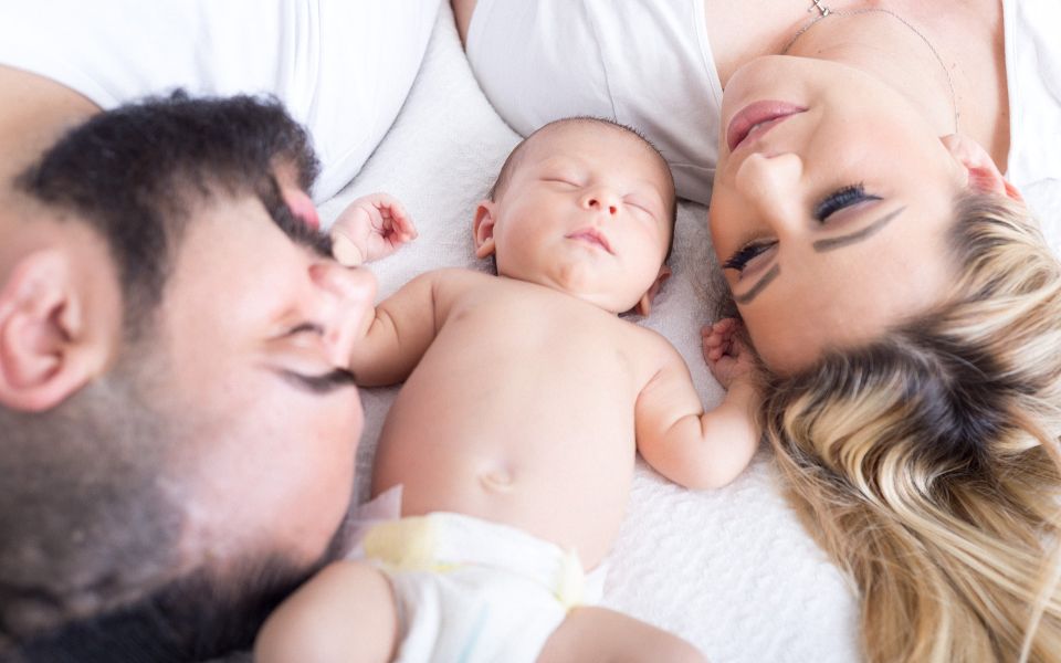 baby op bed tussen gezicht papa en mama